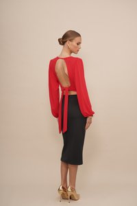 Rood langemouwen top met een open rug en strikdetail, gecombineerd met een aansluitende zwarte midi-rok en gouden hoge hakken. Soepele stoftextuur.