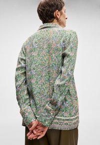 Ανθισμένο πουκάμισο με κουμπιά σε πράσινο χρώμα, με πολύχρωμο σχέδιο που περιλαμβάνει ροζ και μπλε λουλούδια. Με μακριά μανίκια και άνετη εφαρμογή.