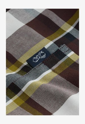 Ruitjesstof met bruine, groene, zwarte en witte kleuren en een gestructureerde weefsel. Inclusief een marineblauw label met witte stikdetails.