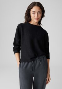 Schwarzer strukturiertes Sweatshirt mit rundem Ausschnitt und dreiviertellangen Ärmeln, kombiniert mit dunkelgrauen Jogginghosen mit Kordelzug. Einfaches und lässiges Design.