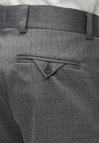 Hallid kohandatud püksid, millel on tekstuuriga ruuduline muster, kolmnurkne tagatasku koos nupuga ja vööaugud vöö kinnitamiseks.