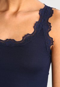 Débardeur côtelé bleu marine avec dentelle au niveau de l'encolure et des bretelles. Texture lisse avec un design ajusté, mettant en valeur la zone de la clavicule.