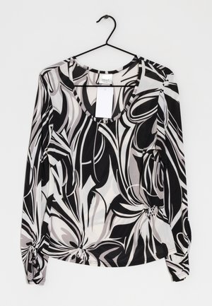 Blusa de manga larga con estampado floral en negro, blanco y gris, con escote redondo, colgada en una percha negra contra un fondo blanco.