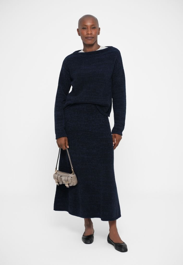 Ensemble en tricot navy composé d'un pull ample et d'une longue jupe. Le modèle porte un petit sac à main gris et des ballerines noires.