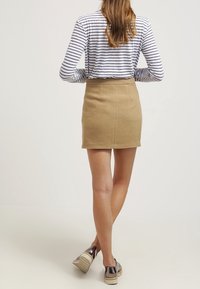 Jupe ajustée beige en tissu texturé, associée à un haut rayé à manches longues ; le mannequin présente une vue de dos avec des chaussures brillantes.