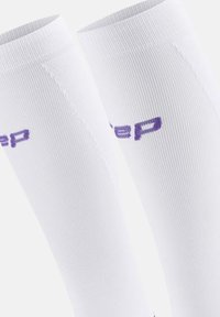 Weiße Kompressionsstrümpfe mit gerippter Textur. Mit einem lila Logo im oberen Bereich bedruckt. Glattes, körpernahes Design.