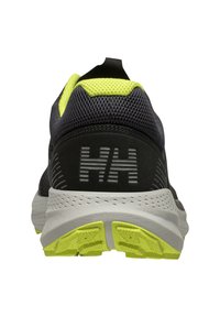 Zapatilla deportiva en negro y gris con parte superior de malla, detalles en amarillo y suela texturizada. Presenta un logo y una marca prominente en el talón.