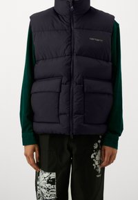 Gilet imbottito navy con colletto alto, chiusura frontale con zip e due ampie tasche, realizzato in materiale trapuntato con una finitura liscia.