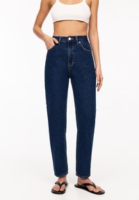 Pantalones vaqueros de tiro alto en azul oscuro con pierna recta, que presentan un cierre frontal de botón, cinco bolsillos y detalles de costura clara.