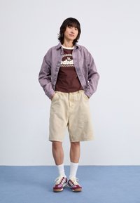 Lavender denim shirt, brown graphic t-shirt, beige shorts, white socks, maroon and white sneakers. Simple, casual outfit with varied textures.