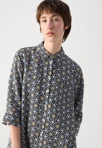 Camicia con bottoni caratterizzata da un motivo nero e bianco di design circolari con accenti gialli. Realizzata in un tessuto leggero con colletto.