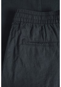 Mörkgrå byxor med elastisk midja, slät textur och en enda bakficka med sömdekoration.