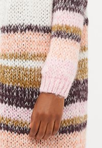 Adītas džemperis ar horizontālām svītrām baltā, rozā, brūnā un violetā krāsā. Mīksta tekstūra ar ribotām piedurknēm un atvērtu adījuma dizainu.