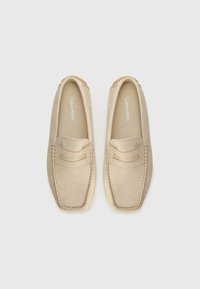 Beige leather loafers with a smooth texture, rounded toe, decorative stitching, and a subtle logo on the insole.