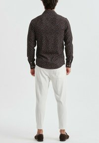 Chemise noire à manches longues avec un motif abstrait coloré, associée à un pantalon texturé blanc et des chaussures marron, vue de l'arrière.