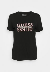 Černé bavlněné tričko s krátkými ohrnutými rukávy, s růžovým logem "GUESS" a dekorativními stříbrnými akcenty kolem textu.