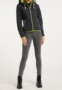 Mörkgrå zip-front jacka med neongröna detaljer och huva, med två framfickor och dragsko-stängningar. Kombination med gråjeans och svarta stövlar.