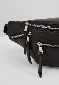 Marsupio in pelle nera con più tasche con zip, accessori in tonalità argento, finitura testurizzata e spallacci regolabili.