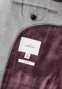 Sivi teksturirani sako iznutra sa bordo uzorkastom podlogom. Oznake ukazuju na "NEXT SIGNATURE", veličina 40R i "SLIM FIT". Detalj s crnim dugmetom.