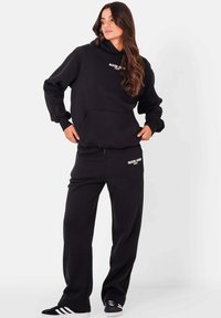 Zwart hoodie en sweatpants set gemaakt van zachte stof, met een voorzak en geborduurd logo in het wit. Casual, relaxte pasvorm.