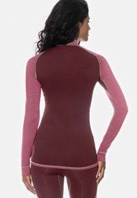 Haut de sport à manches longues en tissu bordeaux et rose, avec des coutures contrastantes et une coupe ajustée, présentant des surfaces lisses et texturées.