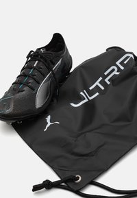 Musta jalkapallokenkä, jossa on teksturoitu päällinen ja turkoosit yksityiskohdat, sekä musta nyörikassi, jossa lukee "ULTRA" valkoisella ja on logo.