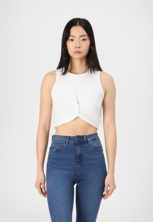 Hvit crop topp med vridd frontdesign, sammen med høyt liv blå denimjeans. Glatt tekstur, tettsittende form og ingen synlige mønstre.