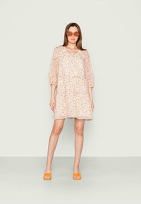 Vestido com padrão floral em rosa claro, com mangas bufantes e decote em V. Acompanhado de óculos de sol laranja e sandálias de slide laranjas.