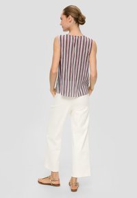 Mouwloos topje met verticale veelkleurige strepen, gemaakt van lichte stof. Gecombineerd met witte wijde broek en sandalen.