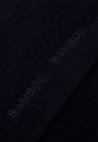 Sciarpa blu scuro realizzata in morbido materiale con una finitura testurizzata. Presenta un discreto ricamo "SAMSØE" in un colore abbinato lungo un bordo.