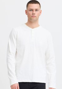 Langärmliges, weißes Henley-Shirt aus weichem Stoff mit V-Ausschnitt und Drei-Knopf-Leiste. Einfaches, strukturiertes Design mit lockerer Passform.