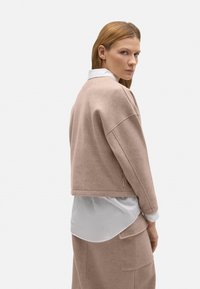 Suéter de lana beige recortado con hombros caídos, combinado con una camisa blanca con cuello. Textura suave y sutiles detalles de costura.