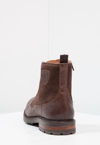 Brun läder- och mockastövlett med rund tå, texturerad klack, dragflik och emblem på sidan. Robust gummisula.