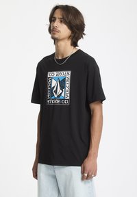 Sort T-shirt med korte ærmer, prydet med et grafisk design i blå og hvid med en rektangulær ramme. Stoffet ser glat ud, casual pasform.