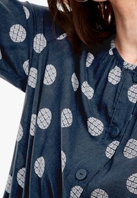 Navy blue shirt with white circular pattern, featuring a button closure and gathered neckline for a relaxed fit.