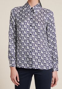 Long-sleeve button-up shirt in navy blue and white with a geometric pattern. Features a collared neck and button placket. Smooth fabric texture.