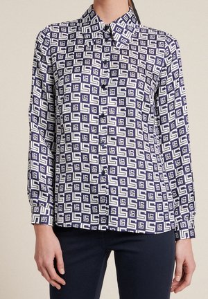 Camicia a maniche lunghe con bottoni in blu navy e bianco con un motivo geometrico. Caratterizzata da colletto e pattina dei bottoni. Tessuto con una texture liscia.