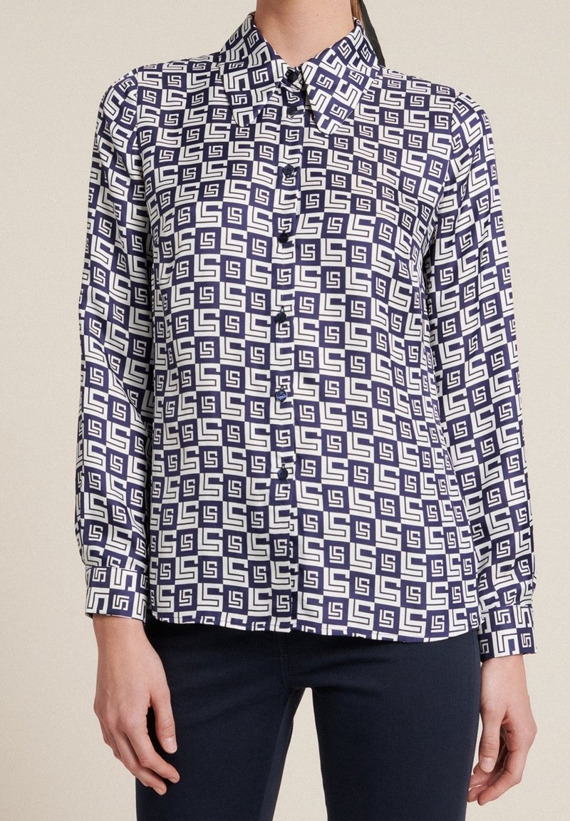 Long-sleeve button-up shirt in navy blue and white with a geometric pattern. Features a collared neck and button placket. Smooth fabric texture.
