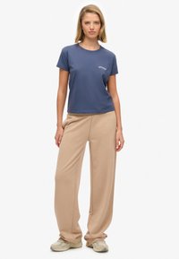 Granatowy bawełniany t-shirt z okrągłym dekoltem i małym białym logo. Beżowe spodnie o szerokich nogawkach, z miękkiego materiału, z bezszwowymi bocznymi detalami. Buty sportowe.