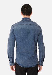 Camicia in denim di un blu medio, con taglio dritto, polsini con bottone e una leggera trama, caratterizzata da dettagli sul yoke posteriore e colletto classico.