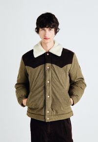 Veste vert olive avec un col en polaire beige, partie supérieure marron, boutons pression, poignets élastiques et une finition douce au toucher.