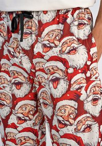 Rode pyjamabroek met een herhaalde print van lachende kerstman gezichten, met witte baarden en rode hoedjes. Zwarte trekkoord bij de tailleband.