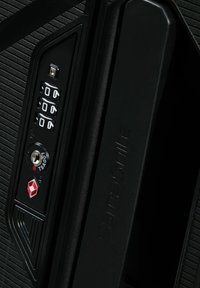 Valise noire avec une surface texturée, serrure à combinaison avec cadran numérique et trou de serrure approuvé par la TSA. Nom de la marque embossé sur la poignée.