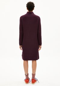 Robe en tricot côtelé violet avec un col haut et des manches longues, dotée de fentes latérales à l'ourlet, associée à des chaussures rouges et des chaussettes en tricot.