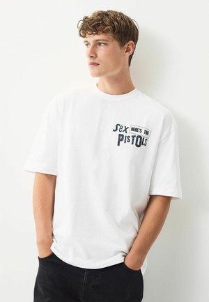 Hvid bomulds T-shirt med en grafik i sort tekst, der står "Sex. Her er pistolerne." Korte ærmer og afslappet pasform.