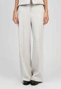 Pantalons beige sur mesure avec une texture lisse, présentant une coupe droite et des jambes larges, agrémentés d'un pli avant subtil.