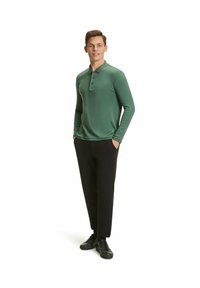 Grünes Langarm-Polohemden mit einem knöpfbaren Kragen, kombiniert mit schwarzen Hosen und schwarzen Sneakers. Glatte Textur und taillierte Passform.