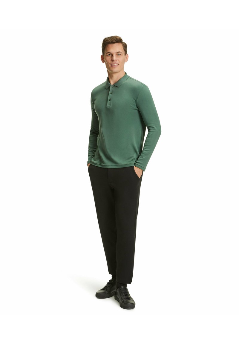Grünes Langarm-Polohemden mit einem knöpfbaren Kragen, kombiniert mit schwarzen Hosen und schwarzen Sneakers. Glatte Textur und taillierte Passform.