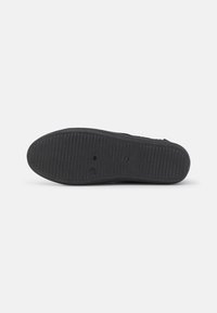 Schwarze Gummisohle mit strukturiertem Grip-Muster, runder Form und zwei runden Lüftungslöchern, mit gerippten Details.