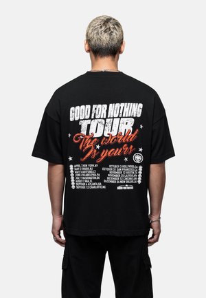 T-shirt noir surdimensionné avec un graphique audacieux en blanc et rouge au dos, affichant les dates de la tournée, des étoiles et le texte "Good for Nothing Tour".